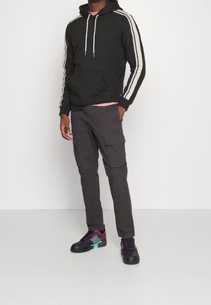 Sweat à capuche noir avec des rayures beiges sur les manches, pantalon cargo gris avec des poches, et baskets noires avec des accents colorés.