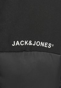 Črna jakna z zgornjim delom z teksturo in gladkim spodnjim delom, s belim logotipom "JACK&JONES".