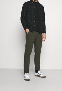 Svart och grön rutigt skjorta över en svart t-shirt, kombinerat med olivgröna byxor och vita sneakers med svarta ränder.