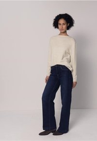 Pull en maille ivoire, coupe décontractée, manches longues. Jean droit bleu foncé, lavage moyen. Chaussures plates marron. Fond clair.