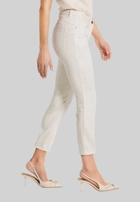 Hellbeige maßgeschneiderte Jeans mit Slim-Fit, hoher Taille und subtiler Textur, kombiniert mit nudefarbenen, hochhackigen Mules, die eine elegante Silhouette betonen.