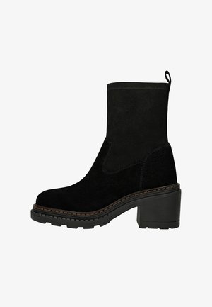 Czarny zamszowy botek na kostkę z blokowym obcasem, teksturowaną cholewką i elastycznymi panelami po bokach. Posiada solidną podeszwę z bieżnikiem i pętelkę do łatwego zakładania.