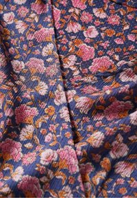 Tessuto floreale con sfondo blu navy, decorato con fiori rosa e arancioni e dettagli intricati. Superficie testurizzata con motivi sottili.