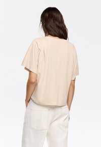 Beige short-sleeve t-shirt with a relaxed fit, round neckline, and soft cotton material. Back features a plain design without notable accents.