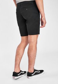 Shorts in cotone nero con una vestibilità slim, dotati di due tasche posteriori e chiusura con bottone. Indossati con sneakers nere e bianche.