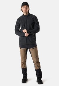 Mörkgrå fleecejacka med framdragkedja, i kombination med bruna och svarta friluftsbyxor med dragkedjefickor. Hållbar och funktionell design.