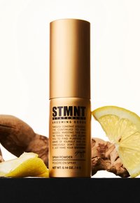 Guld cylindrisk sprayflaska märkt "STMNT Statement Grooming Goods" bredvid en citronskiva och en bit trä. Kapacitet 0,14 oz.