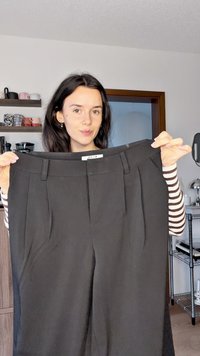 Juodos siuvinėtų kelnių priekiniai klostes, plokščias juosmuo ir šoninės kišenės. Pagamintos iš lygios medžiagos, jas laiko dėvintis asmuo su dryžuotomis rankovėmis.