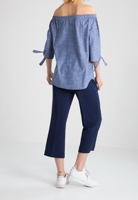 Blå off-shoulder top med trekvart lange ærmer og bindebånd, parret med marineblå cropped bukser og hvide sneakers. Teksturstof i let materiale.