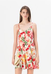 Abito floreale con sfondo crema, caratterizzato da grandi fiori rossi e gialli. Spalline sottili, scollatura a V e gonna svasata. In mano una borsa a tracolla intrecciata.