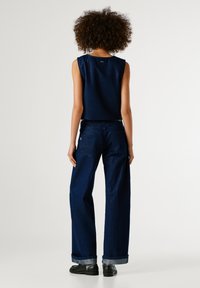 Tmavomodré džínsy so voľným strihom, s vyhrnutými manžetami a zadnými vreckami, spárované s ladným bezrukávovým topom.