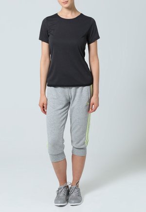 Mustat lyhythihaiset urheilupaidat yhdistettyinä harmaisiin lyhyisiin collegehousuihin, joissa on keltaiset sivuviivat. Päällä harmaat urheilukengät.