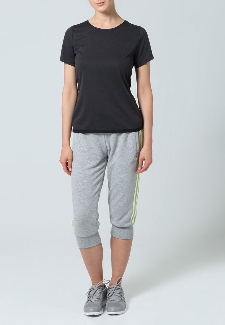 Svart kortärmad tränings T-shirt i kombination med grå avklippta träningsbyxor med gula sidostråk. Bärs med grå träningssneakers.