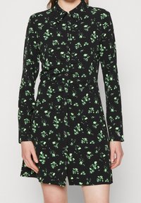 Czarna sukienka z długimi rękawami, zielony wzór kwiatowy, zapięcie na guziki i kołnierzyk. Miękka tkanina z lekkim połyskiem.