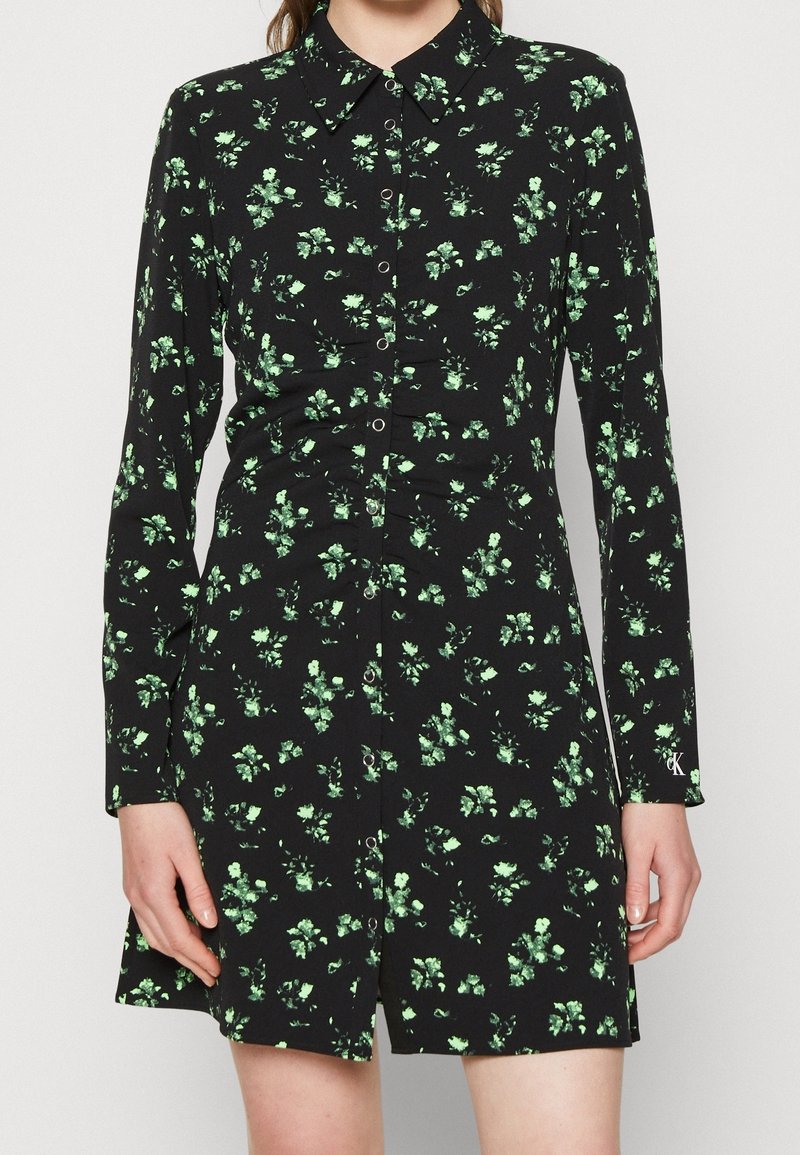 Czarna sukienka z długimi rękawami, zielony wzór kwiatowy, zapięcie na guziki i kołnierzyk. Miękka tkanina z lekkim połyskiem.