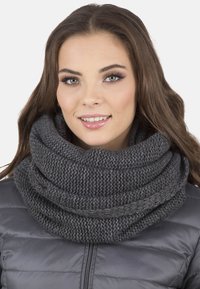 Pletený šedý nekonečný šátek s hustým, strukturovaným vzorem. Nošený volně, ukazuje útulný a objemný design. Vhodný pro nošení v chladném počasí.