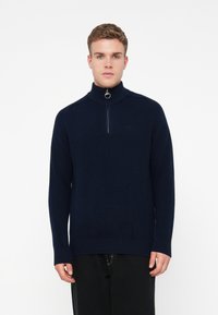 Maglione con zip al collo in un morbido tessuto a maglia di colore blu navy. Presenta un colletto e polsini a costine, una mezza zip e un discreto logo sul petto.