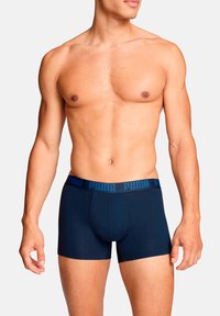 Marineblaue Boxershorts mit einem breiten blauen Bund, der das geprägte "PUMA"-Logo zeigt. Hergestellt aus glattem, elastischem Material. Die Shorts haben eine eng anliegende Passform.