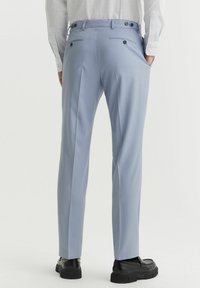 Jasnoniebieskie spersonalizowane spodnie o gładkiej teksturze, z tylnymi kieszeniami i guzikami. Nogawki mają slim fit, zwężając się ku kostce.