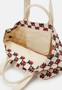 Sac fourre-tout en toile avec un intérieur beige, ornée d'un biais à motifs d'éléments graphiques noirs et rouges. Comprend une poche latérale pour le rangement.