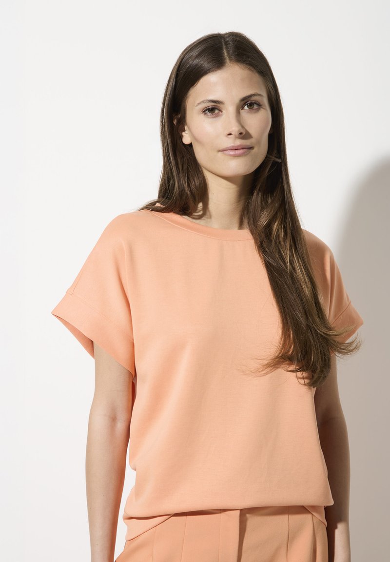 Perzikkleurige T-shirt met korte mouwen en een losse pasvorm, gemaakt van zachte stof, heeft een ronde halslijn en een gladde textuur.