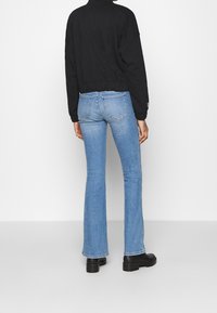 Svart kort sweatshirt och ljusblå utsvängda jeans. Jeansen har två bakfickor och lätt blekning. Svarta klumpiga stövlar fulländar looken.