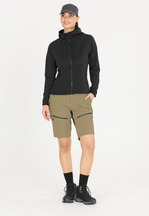 Haut de hoodie noir avec fermeture éclair et texture, shorts vert olive avec poches zippées, bottes de randonnée noires et casquette grise.