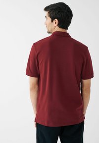 Bordo polo majica s mekim materijalom, kratkim rukavima i ravnim ovratnikom. Stražnji dio je malo dulji, s čistim linijama i minimalnim dizajnom.