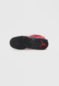 Czerwona i czarna podeszwa buta do koszykówki z okrągłymi wzorami antypoślizgowymi oraz czerwonym logo Jumpman na białym tle.