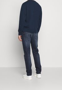 Felpa blu navy con collo rotondo, abbinata a jeans in denim scuro. Scarpe da ginnastica bianche completano il look. Design semplice e casual.