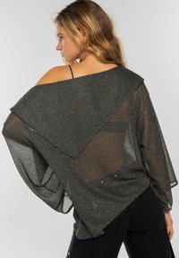 Top de tela negra y transparente con espalda drapeada, textura brillante y mangas anchas. Diseño en capas que añade dimensión.