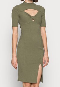 Robe côtelée vert olive avec manches courtes, col montant et détail torsadé à la taille. Dotée d'une fente latérale et d'accents découpés.