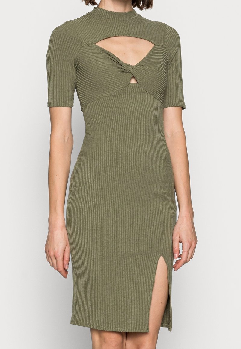 Robe côtelée vert olive avec manches courtes, col montant et détail torsadé à la taille. Dotée d'une fente latérale et d'accents découpés.