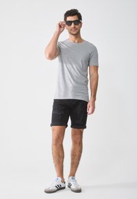 Gray short-sleeve t-shirt paired with black denim shorts featuring distressed accents, and white sneakers with black stripes.