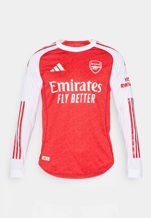 Maglia a maniche lunghe rossa con texture a motivo, maniche bianche e righe rosse. Presenta il logo dell'Arsenal e il testo "Emirates Fly Better".