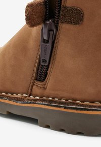 Bottine en daim marron avec fermeture éclair, coutures contrastées et semelle en caoutchouc avec un motif texturé pour l'adhérence.