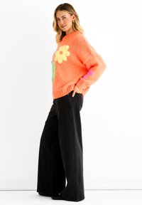 Orange knitted sweater with oversized floral appliqués in yellow, pink, and green; paired with black wide-leg pants.