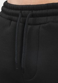 Sorte sweatpants i bomuld med elastisk talje, snorjustering og sidelomme. Stoffet har en blød, struktureret overflade.