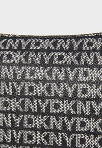 Μαύρος και άσπρος υφασμάτινος ιστός με επαναλαμβανόμενο μοτίβο κειμένου "KNYD" σε διάφορα μεγέθη. Δομημένος, με λεία υφή και λεπτό σχεδιασμό.