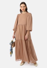 Robes maxi légères de couleur brun clair en chiffon, avec des manches bouffantes, un design à volants et une coupe ample. Assortie à un petit sac à main et une écharpe imprimée.