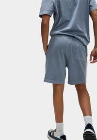 Blaue Baumwollshorts mit lässiger Passform, elastischem Bund, Seiten- und Gesäßtasche; kombiniert mit einem passenden blauen T-Shirt und Sneakers.