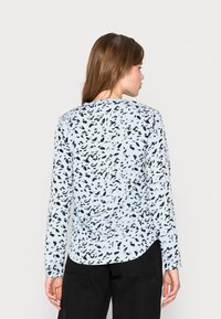 Hellblauses Langarmhemd mit einem schwarzen abstrakten Muster, abgerundetem Saum und weicher Textur, kombiniert mit schwarzen Hosen.
