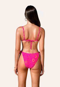 Bikini rosa con un patrón de sol, tirantes ajustables y lazos en los lados. Textura suave, destacando colores brillantes y un diseño juguetón.