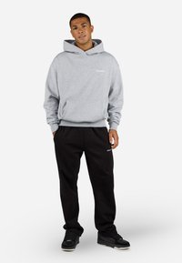 Grå hettegenser med frontlomme og hvit logodetalj, sammen med svarte joggebukser, skaper et uformelt, avslappet antrekk. Svarte sneakers fullfører stilen.