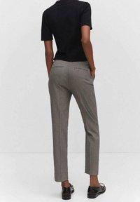 Zwart kortermig topje gecombineerd met nauwsluitende geruite broek in grijs en zwart, met achterzakken en rechte pijpen. Zwarte loafers maken de look compleet.