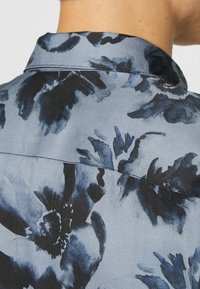 Gros plan sur le dos d'une chemise bleue à motif floral en nuances sombres et claires, montrant le col et la couture supérieure du dos.