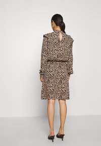 Vestido de estampado de leopardo en beige y negro, con un escote en forma de llave en la parte de atrás, hombros con volantes y cintura ajustada. Tejido suave, diseño hasta la rodilla.
