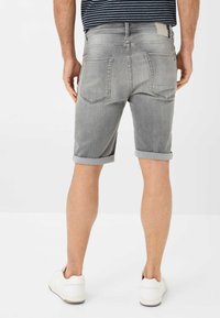 Shorts en denim gris avec un ourlet retroussé, des poches arrière et une texture légèrement décolorée. Portés avec des chaussures de sport blanches.