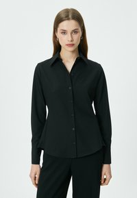 Zwarte lange mouwen shirt van gladde stof, met een puntige kraag, knoopsluiting aan de voorkant en een licht uitlopende zoom.