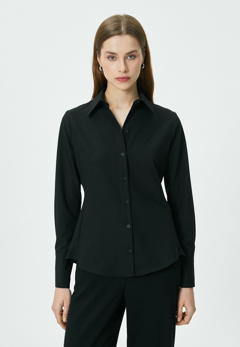 Zwarte lange mouwen shirt van gladde stof, met een puntige kraag, knoopsluiting aan de voorkant en een licht uitlopende zoom.
